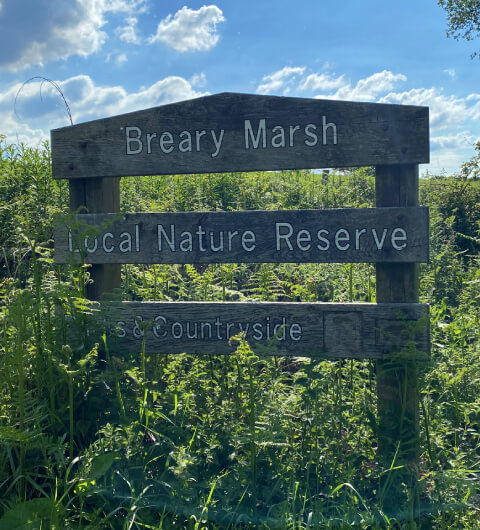 Breary Marsh entrance sign against a blue sky and grass