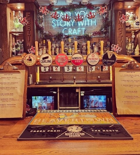 Wooden bar counter at Editor's Draught with a variety of beer taps, including Carling, Amstel, and Guinness, and a decorative mirror with the text "Stock with Story Craft" in the background.