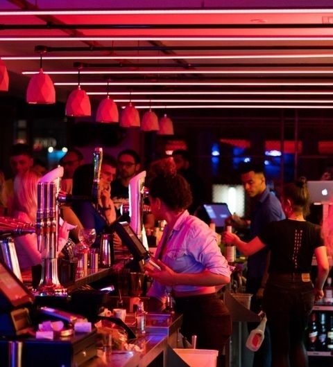 Vibrant atmosphere at Bar Soba with patrons and staff, neon lighting, and a busy bar area.