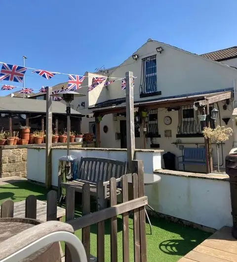 Sunny outdoor seating area at Fox & Grapes with British flags, wooden benches, and potted plants.