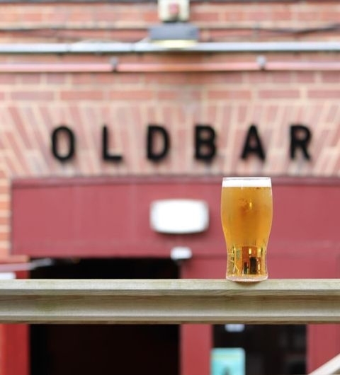 A refreshing pint of beer on a wooden railing with the sign 'OLDBAR' in the background at Old Bar – Leeds Uni.
