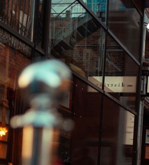 Reflective view of Distrikt entrance with glass facade and blurred foreground railing.