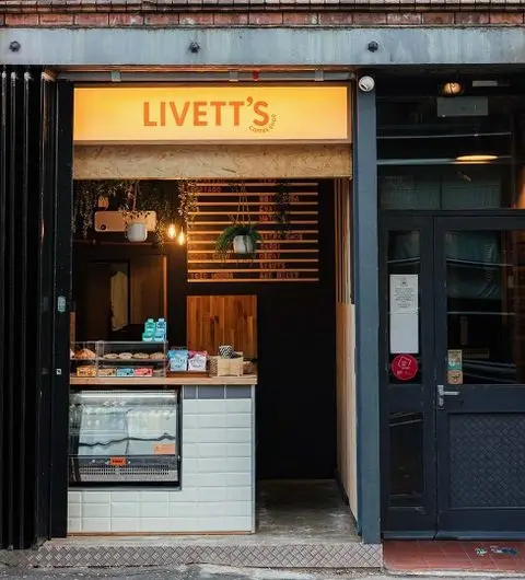 Exterior view of Livett's Coffee Shop with illuminated signage, display case with pastries, and cozy interior visible through the open door.