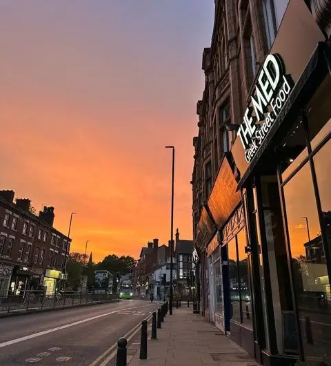 Exterior view of The Med Greek Street Food restaurant at twilight with a vibrant orange sky.