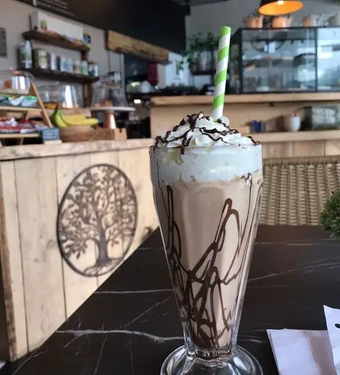 Chocolate milkshake with whipped cream and chocolate syrup in a tall glass with a striped straw, on a table at a cozy cafe in Forista.