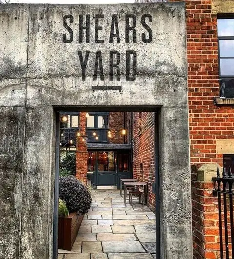 Entrance to Shears Yard with concrete signage above an archway leading to a brick building with outdoor seating.