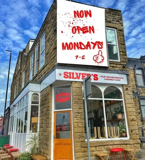 Exterior view of Silver's Deli, a neighborhood sandwich shop with a red and white sign announcing "Now Open Mondays 9-2", set against a blue sky with clouds.