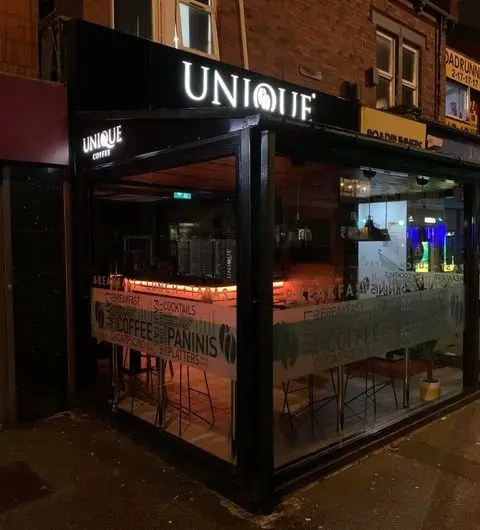 Exterior night view of Unique Coffee&Bistro with illuminated signage, showcasing its glass facade and cozy interior lighting.