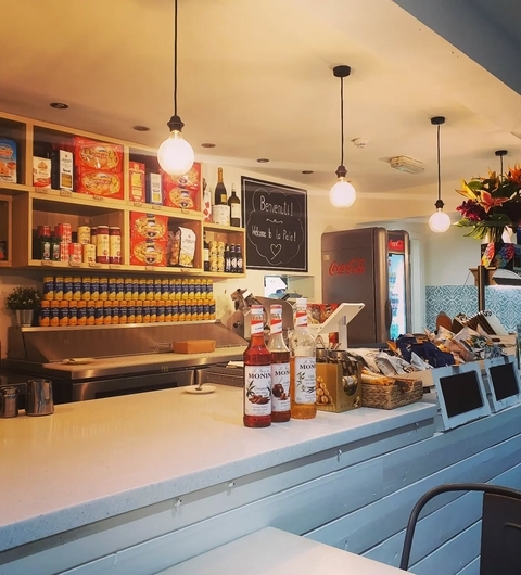 Bright, inviting bar area with shelves of Italian products, hanging lights, and a display of colorful beverages.
