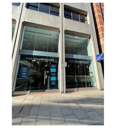 Modern glass facade of The Clubhouse Coffee Leeds, featuring large windows and a welcoming entrance with outdoor seating.