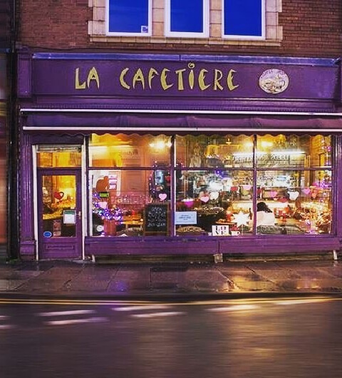 Charming purple storefront of La Cafetiere, warmly lit with cozy seating and heart decorations in the windows.