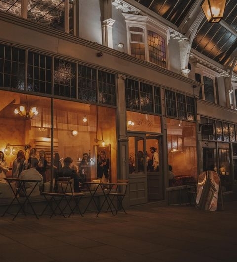Evening view of Sonder, a warmly lit café with patrons inside, featuring large windows and a classic facade under a glass-covered arcade.