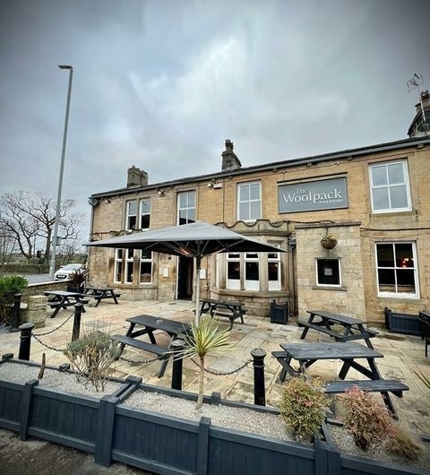 Exterior view of Woolpack Inn with outdoor seating and a large umbrella, set against a cloudy sky.
