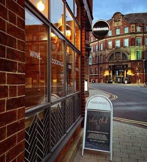 Exterior view of Farrands Bar at twilight with illuminated signage, showcasing wine and cocktails, and a sidewalk sign promoting a wine club.