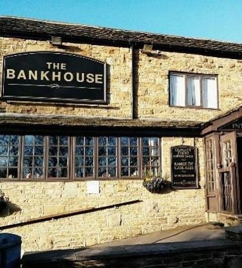 Exterior view of the Bankhouse Inn, showing a traditional stone building with a black signboard, large windows, and a clear blue sky above.