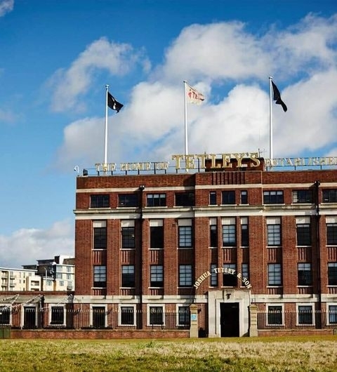 Exterior view of The Tetley, a brick building with large windows and flags flying atop, under a blue sky with scattered clouds.