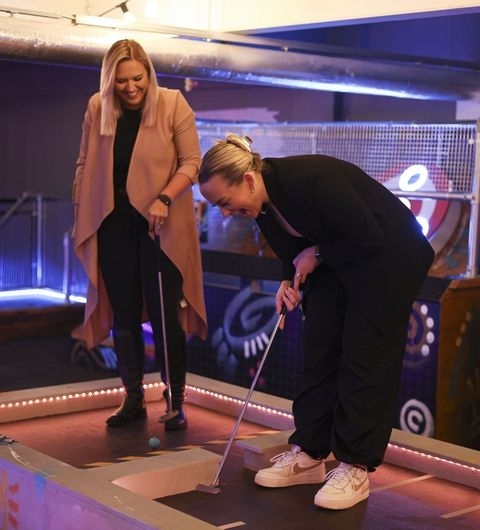 Two people enjoying a game of mini-golf at Boom Battle Bar with neon-lit decor.