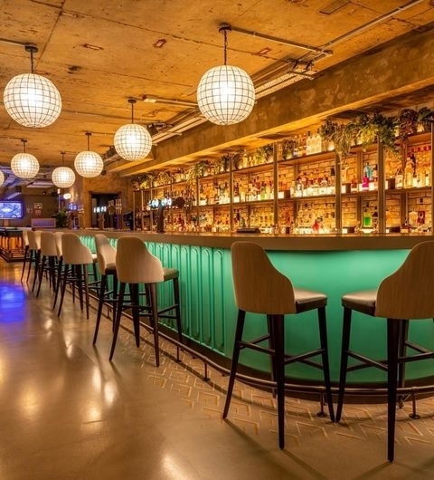 Interior of Electric Shuffle showing a well-lit bar with illuminated shelves of bottles, high stools, and hanging globe lights.