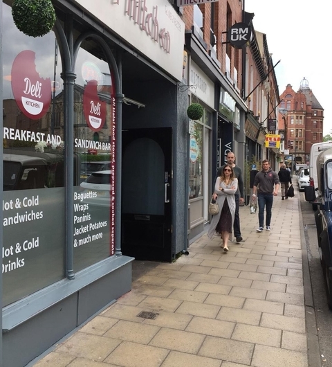 Charming street view of Deli Kitchen, featuring outdoor seating and pedestrians strolling past shops on a lively day.