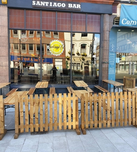 Outdoor seating area at Santiago Bar with wooden tables and a fenced patio, inviting atmosphere in a vibrant urban setting.