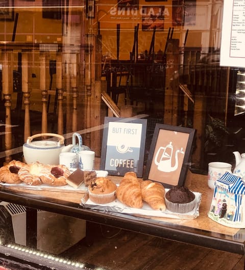 Window display at Chichini showing fresh croissants, muffins, and a But First Coffee sign