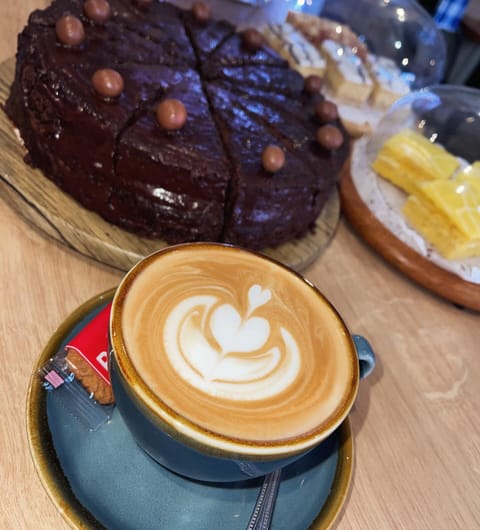 Rich chocolate cake and latte with heart art in a blue cup at Country Crust Leeds