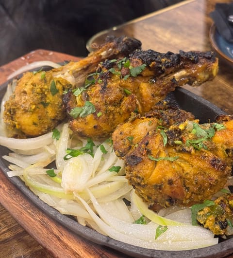 Tandoori chicken legs on a sizzler plate with onions at Mojo Royal Treat Leeds