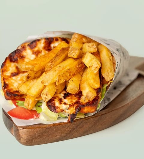 Gyros wrap in branded Yiros paper with skin-on fries on a wooden board