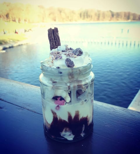 A layered dessert in a glass jar with cream and chocolate flake, with Roundhay Park lake shimmering in the background