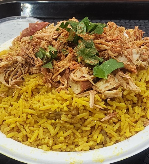 A plate of chicken biryani at Leziza, Leeds, with shredded chicken, spice rub and fresh coriander piled on yellow basmati rice.