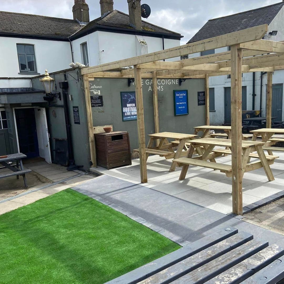 Outdoor seating area at Gascoigne Arms with wooden picnic benches, artificial grass, and a pergola under construction.