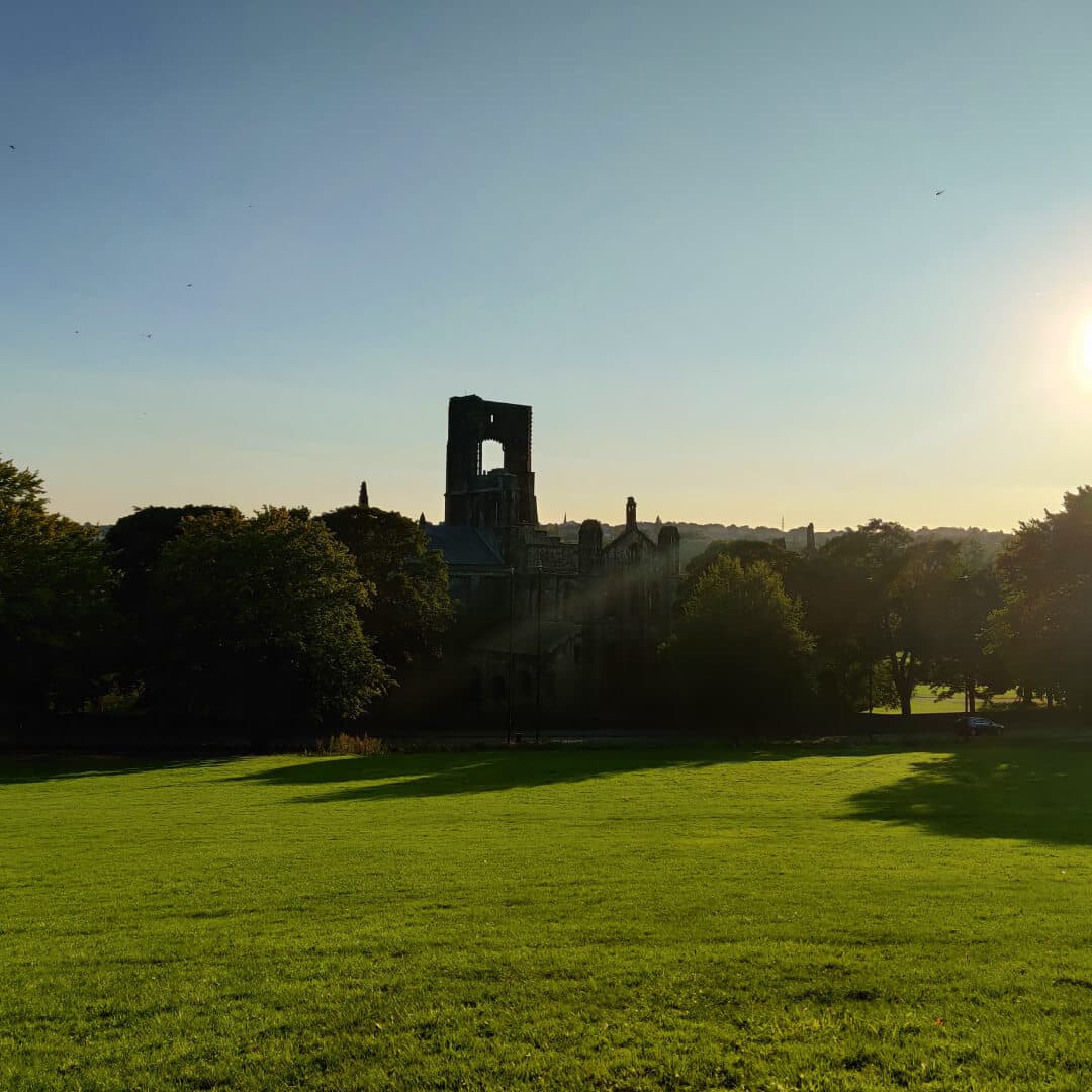 Kirkstall Abbey from a distance over a field in the evening