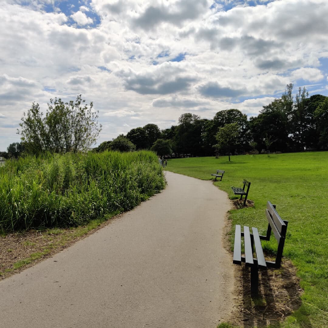 Large path leading around the edge of Yeadon Tarn lake with benches and green grass to the right