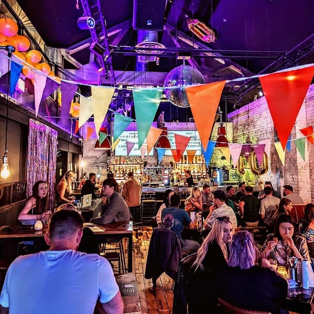 Vibrant interior of Almost Famous with patrons dining and socializing, colorful bunting hanging overhead, and a lively bar area in the background.