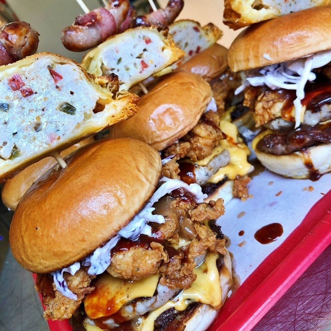 Assorted gourmet burgers and sausages from Almost Famous, showcasing a variety of toppings and sauces on a serving tray.