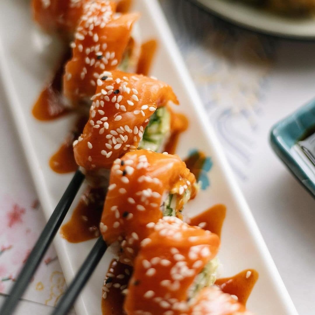 Delicious salmon sushi rolls topped with sesame seeds and drizzled with sauce, served at Blue Sakura.