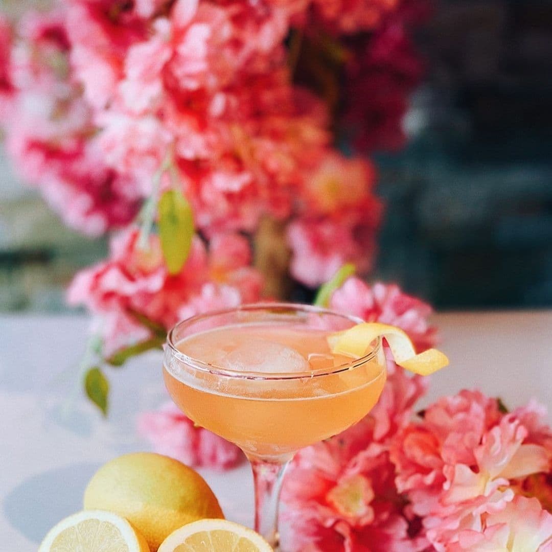 Refreshing cocktail with lemon garnish at Blue Sakura surrounded by vibrant pink blossoms and fresh lemons.