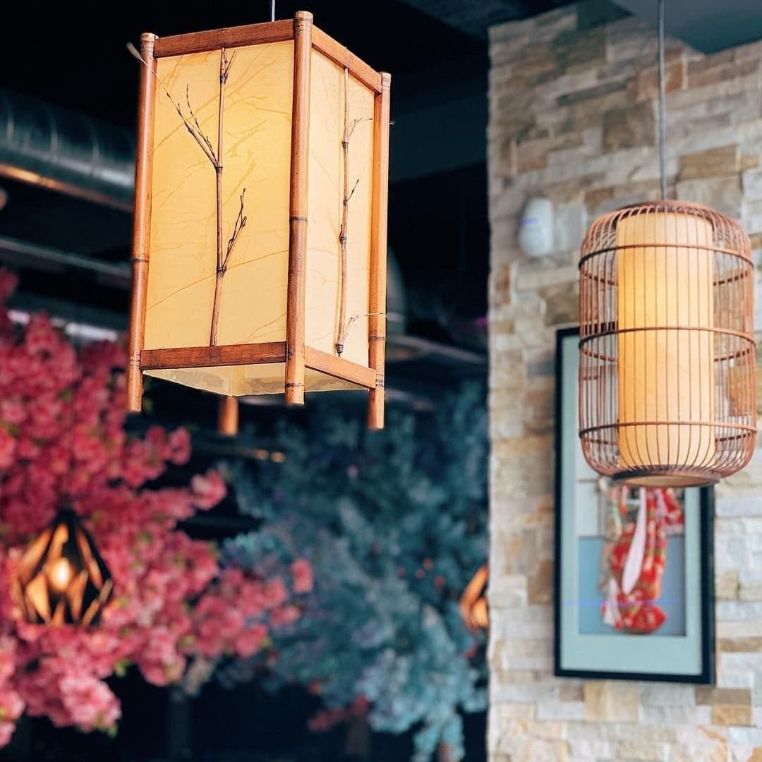 Traditional-style lanterns hanging at Blue Sakura, with a backdrop of cherry blossom trees and a stone wall.