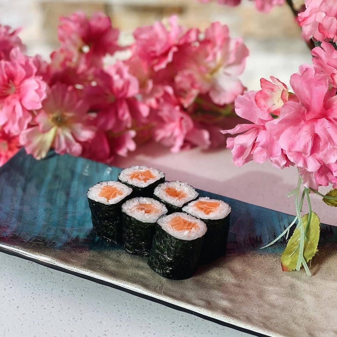 Salmon sushi rolls on a plate at Blue Sakura with pink cherry blossoms in the background.