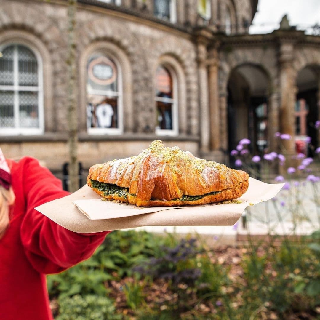 Person holding a delicious-looking bruschetta sandwich with a pesto topping, in front of a historic building with arched windows at Bruschetta.
