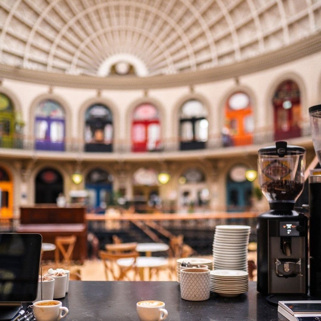 Interior of Bruschetta featuring a coffee bar with espresso cups in the foreground and an elegant dome ceiling above a spacious dining area with colorful storefronts in the background.