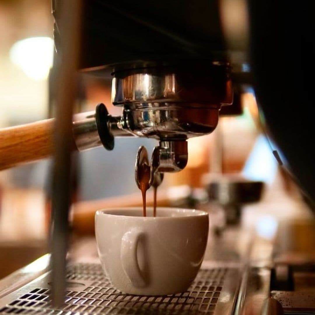 Espresso being brewed into a white cup at Bruschetta, with the coffee machine's portafilter and handle in view.