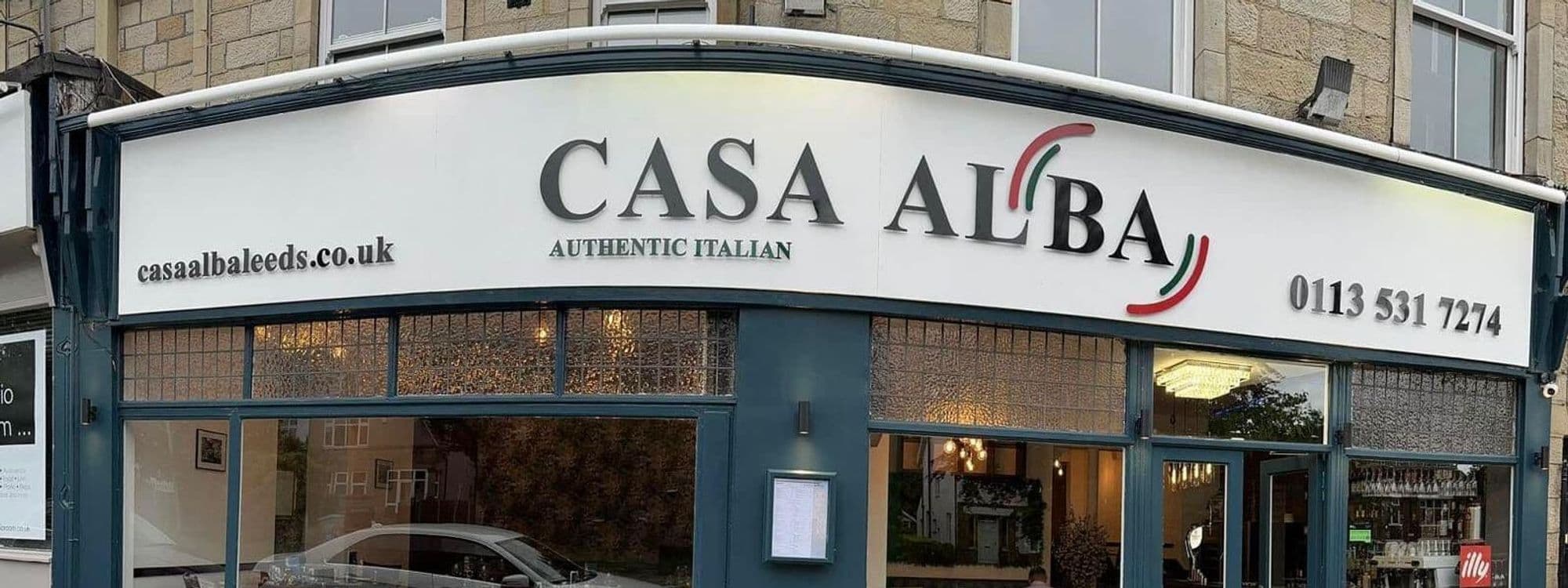 Exterior view of Casa Alba, an authentic Italian restaurant with a white signboard and Italian flag colors, featuring large windows and a blue facade.