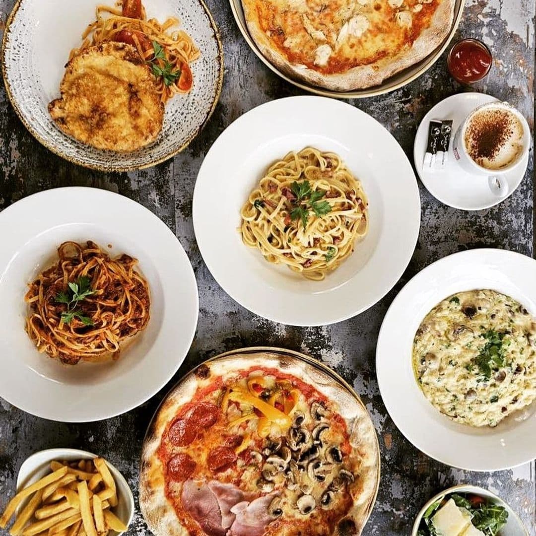Assorted Italian dishes on a table at Casa Alba, featuring pasta, pizza, and a cup of cappuccino.