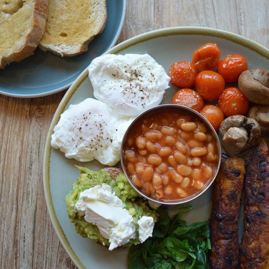 Hearty breakfast platter at Cha Lounge featuring poached eggs, baked beans, roasted tomatoes, sautéed mushrooms, avocado toast with cream cheese, sausages, and toasted bread.