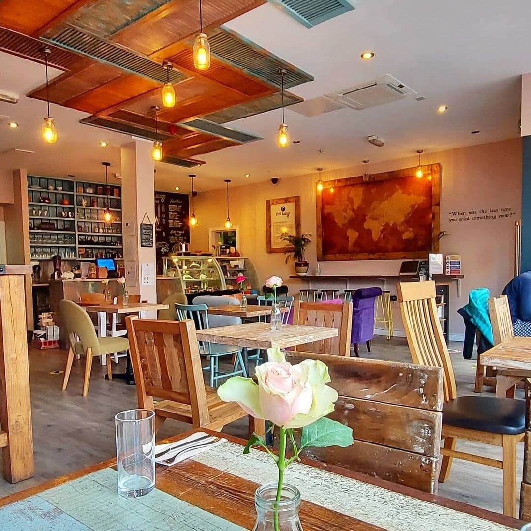 Interior of Cha Lounge featuring wooden tables and chairs, warm hanging lights, a world map artwork on the wall, and a cozy atmosphere with a pale pink rose in the foreground.