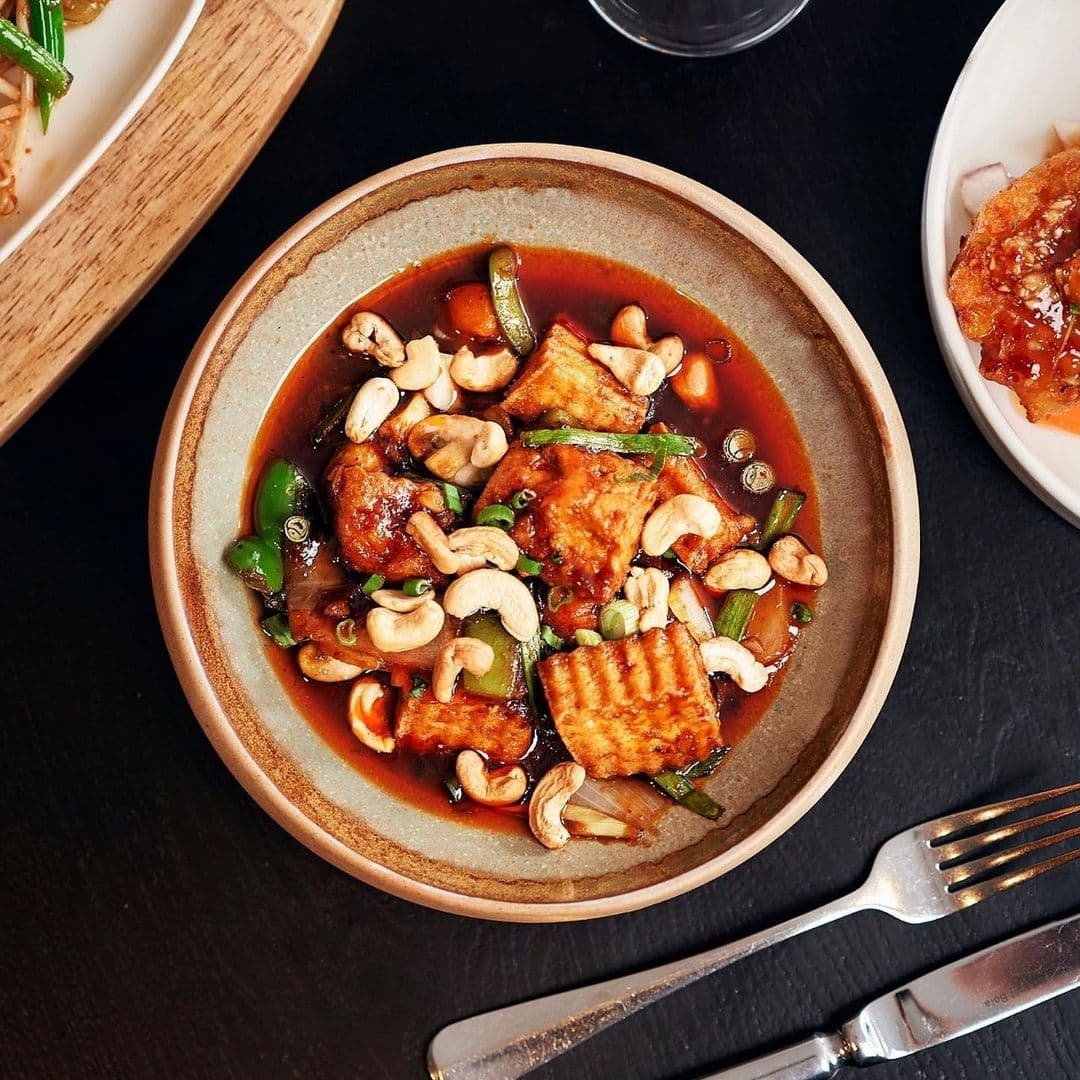 Delicious Thai-style tofu stir-fry with cashew nuts and green onions, served in a brown ceramic bowl at Chaophraya.