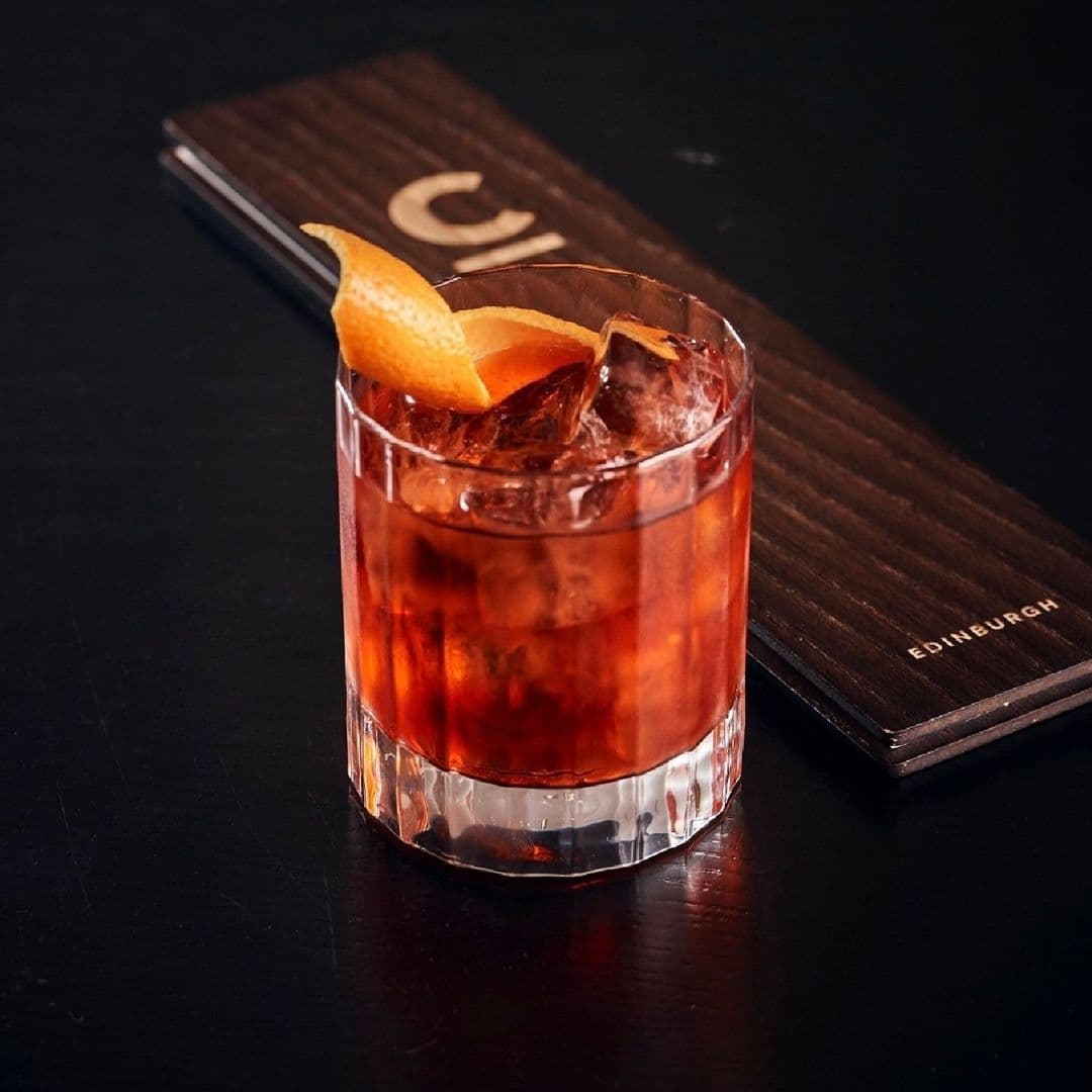A refreshing cocktail with ice and an orange peel garnish, served at Chaophraya, with a dark wooden menu in the background.
