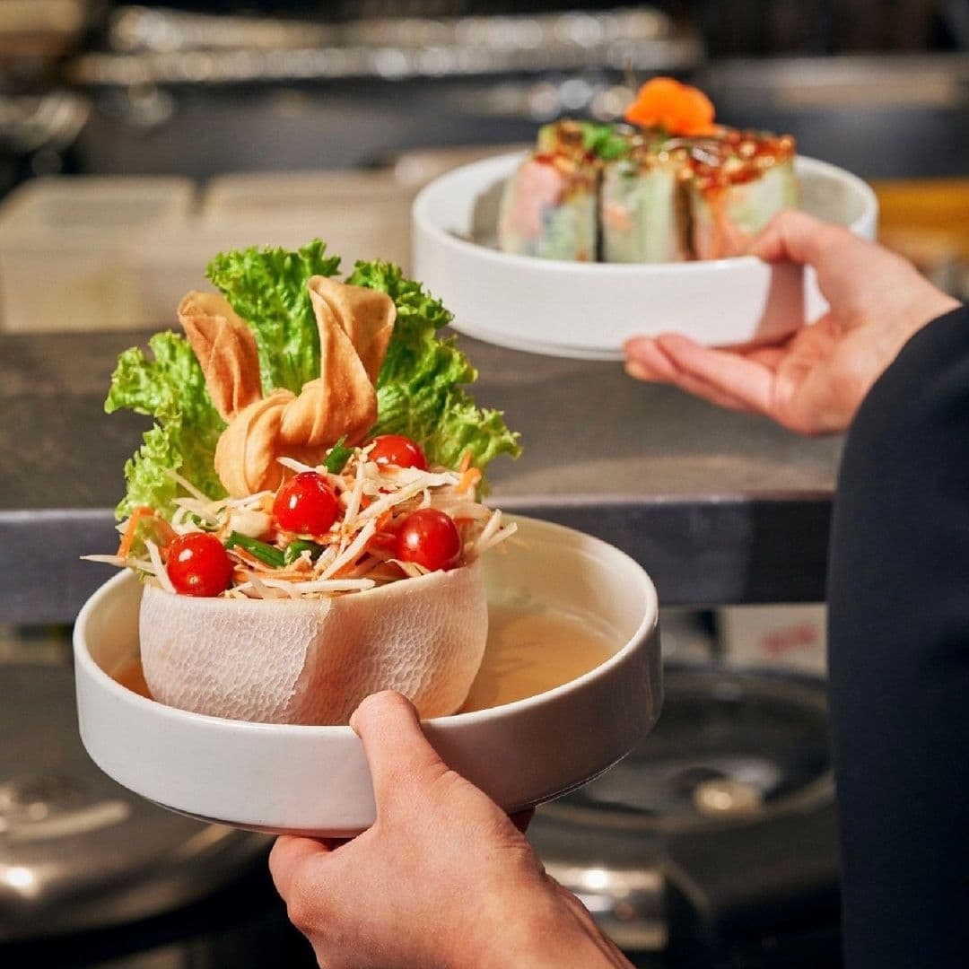 "Fresh Thai salad served in a coconut shell bowl and colorful spring rolls presented on a white plate at Chaophraya."