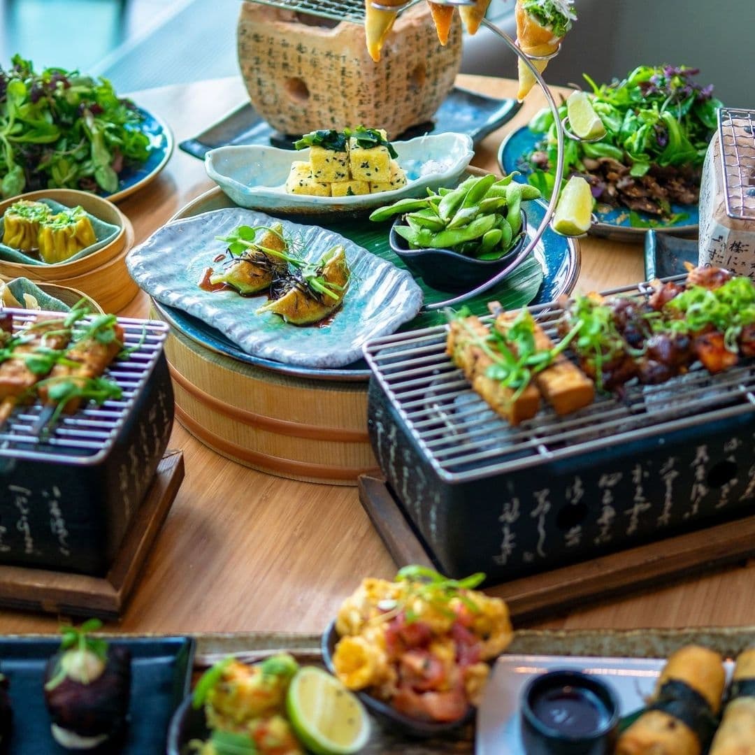 Assorted Asian fusion dishes displayed on a table at Chino Latino, featuring sushi rolls, dumplings, grilled skewers, edamame, and other appetizers, artfully presented on various plates and trays.